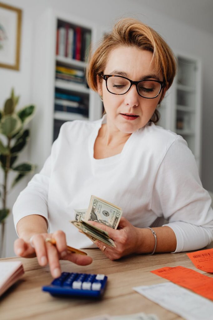 Woman using calculator and handling cash for financial planning at home.